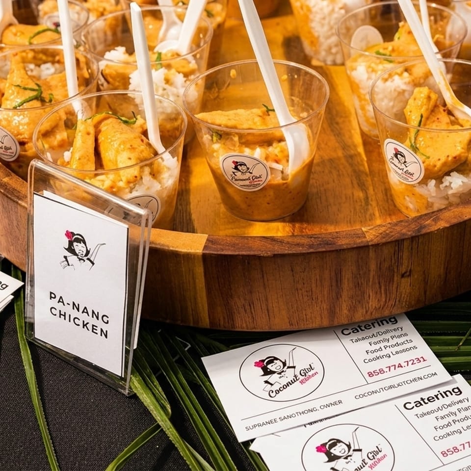 Pa-Nang Chicken samples in small cups with business cards on a wooden tray and palm leaves.