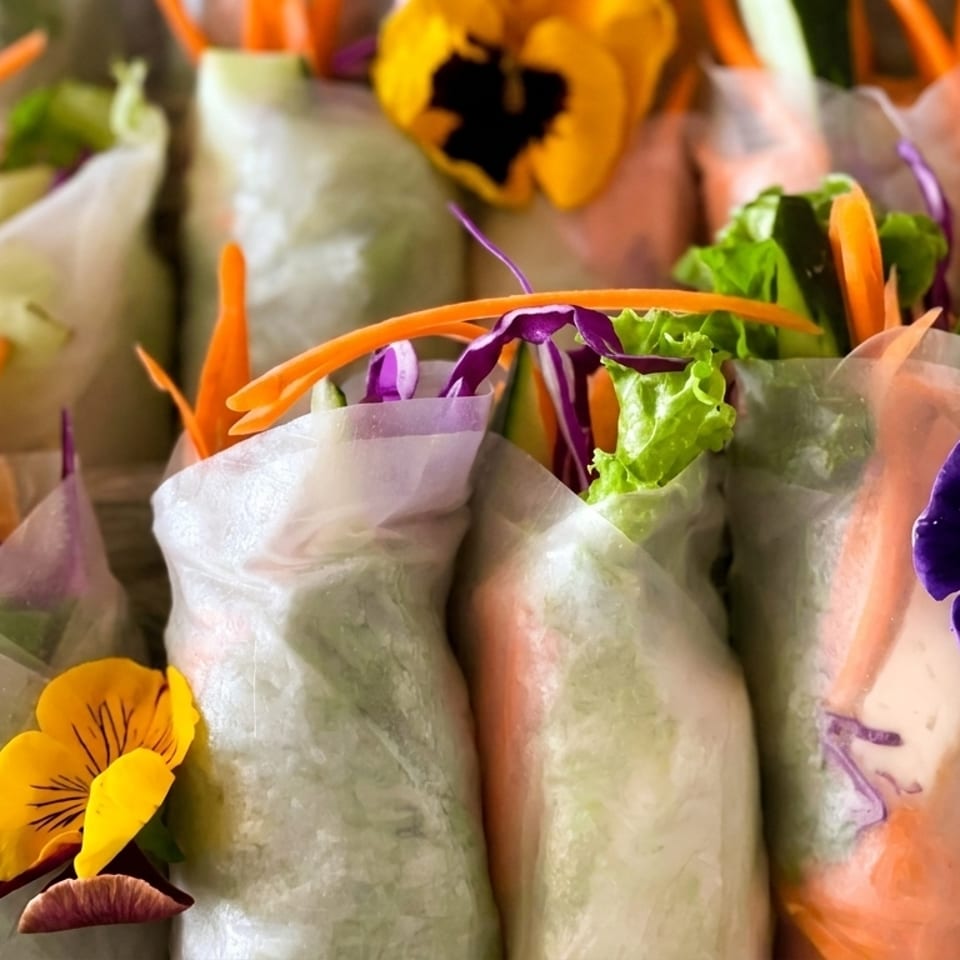 Fresh spring rolls filled with lettuce, carrots, cucumber, and purple cabbage, garnished with edible flowers.